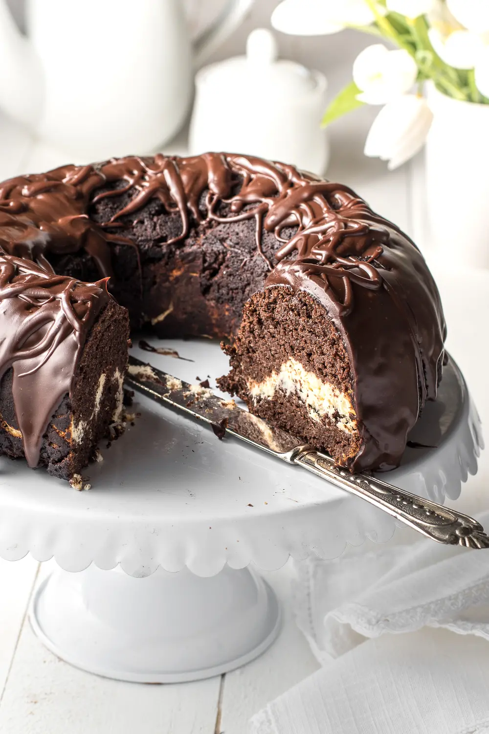 A sliced Chocolate bundt cake on a white cake stand on a white background