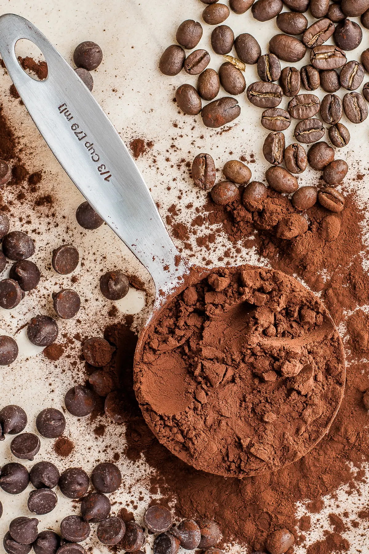 measuring cup with dark cocoa powder surrounded by dark chocolate chips and roasted coffee beans