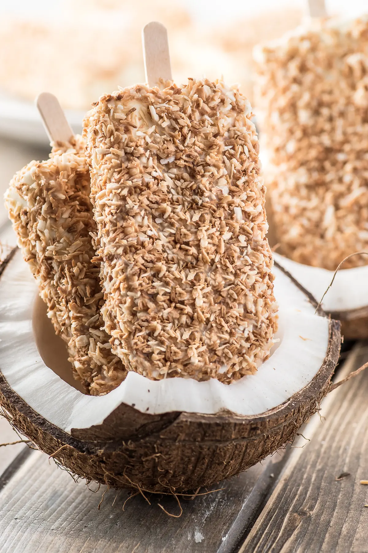 Toasted coconut cream popsicles displayed inside of a cracked fresh coconut
