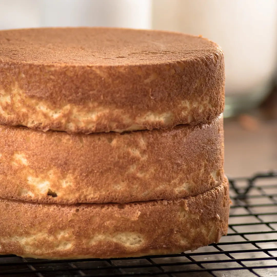 Three golden brown cake layers stacked on top of one another on a black wire cooling rack. 