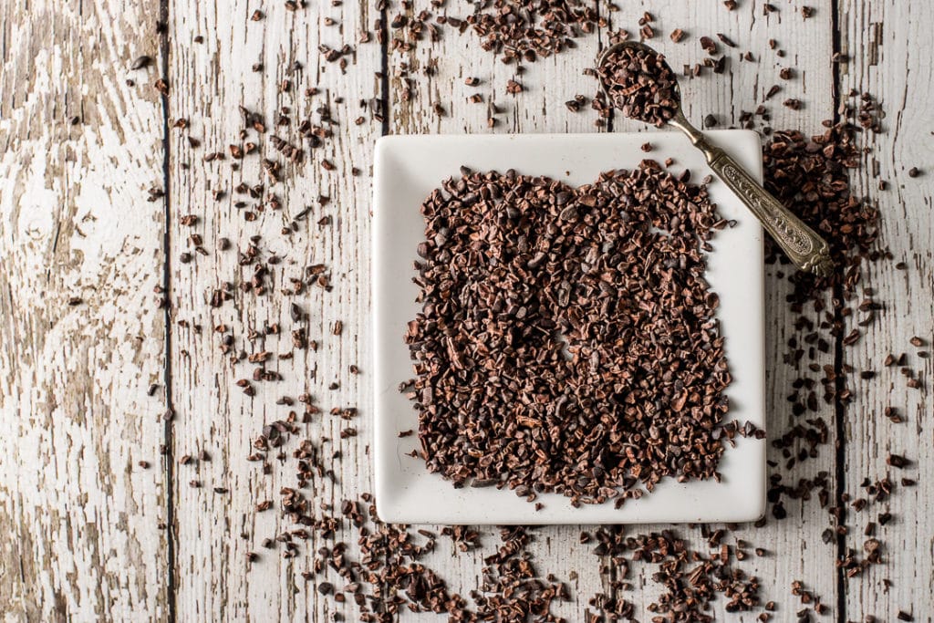 a small square plate filled with dark brown cocoa nips on a wooden background