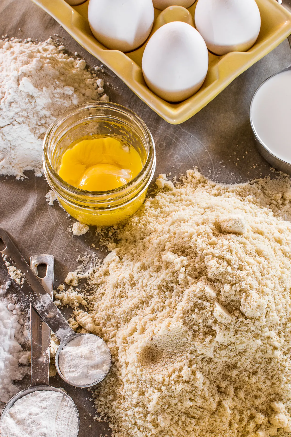 A table of baking ingredients with flours, eggs, and measuring spoons
