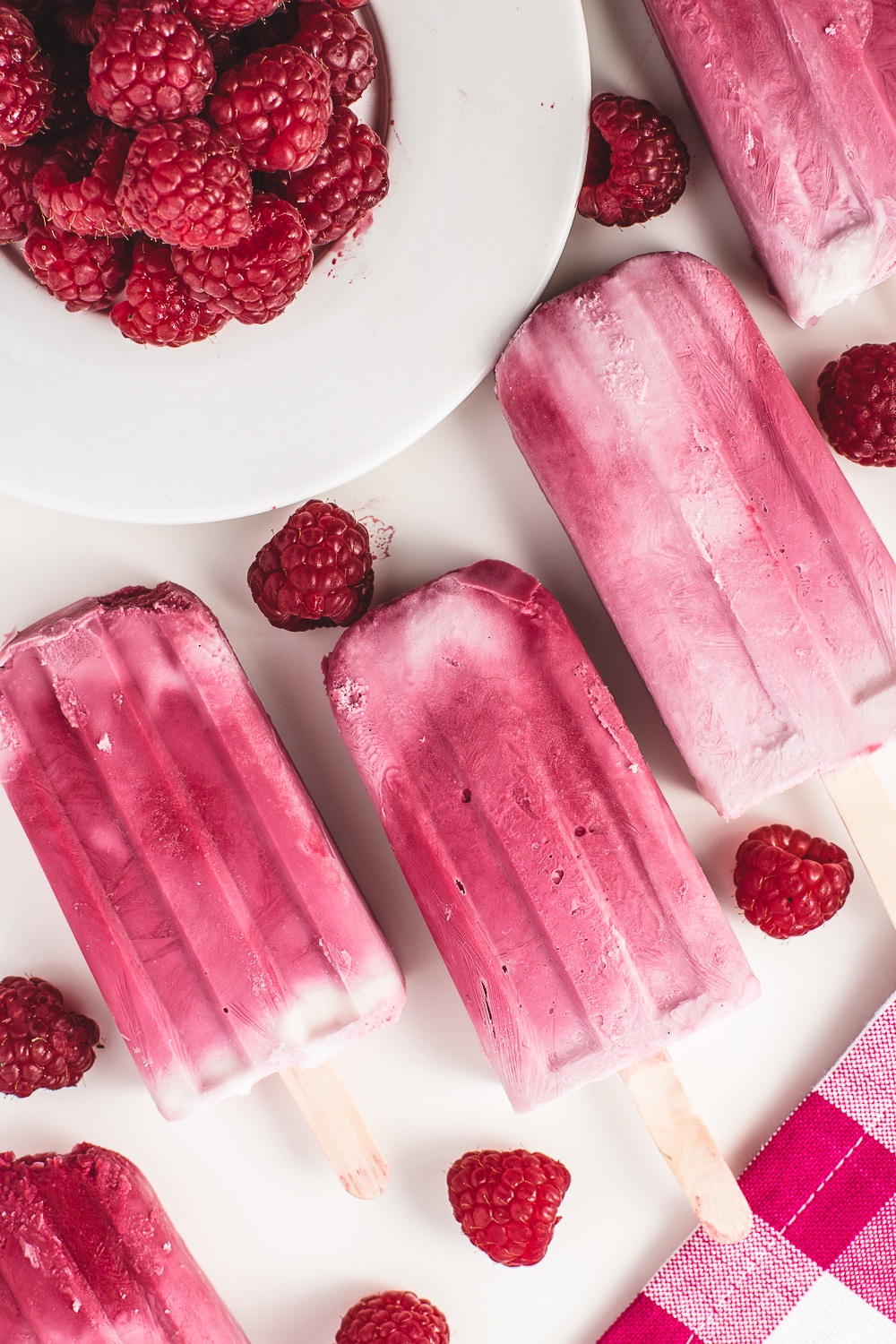 top down photo of bright pink raspberry ripple ice cream bars and a bowl of fresh raspberries