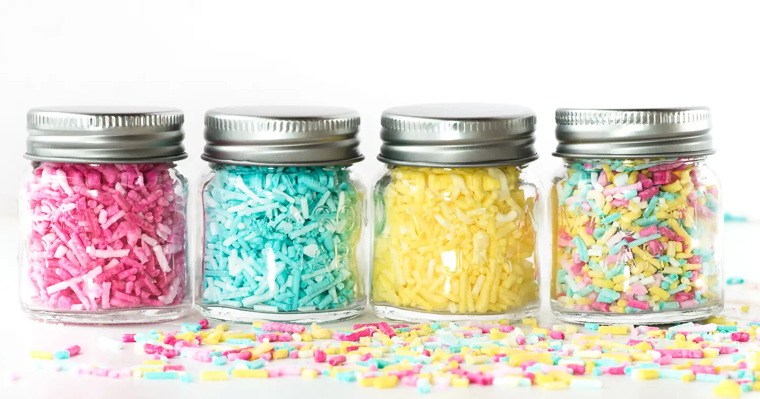 Four jars in a row filled with colourful ombre sprinkles 