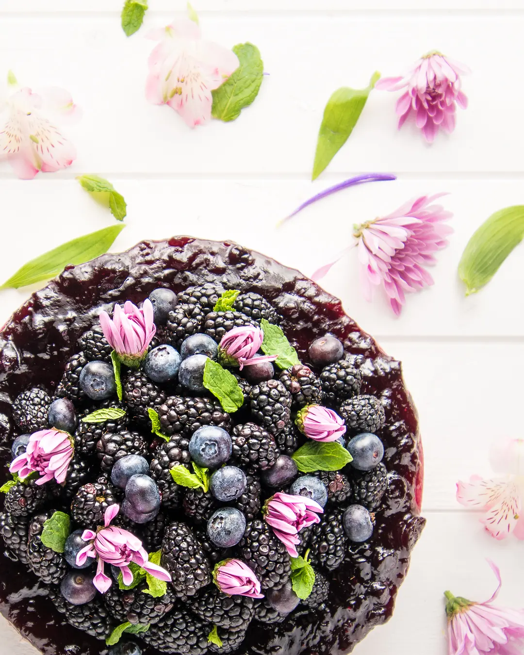 Overhead photograph of a berry cheesecake with sprigs of mint and pink flowers