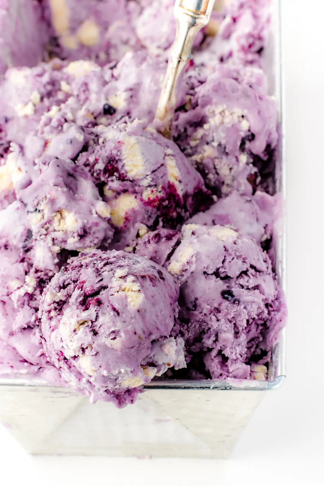Bright lavender coloured blueberry ice cream in a silver loaf pan on a bright white background. 