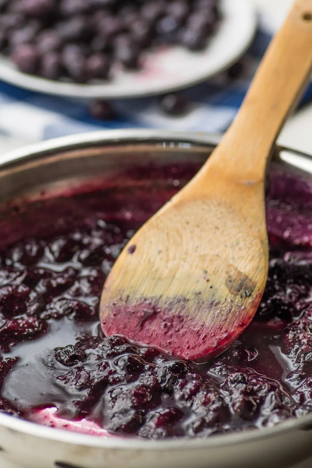 A silver sauce pan with cooked blueberries and a wooden spoon 