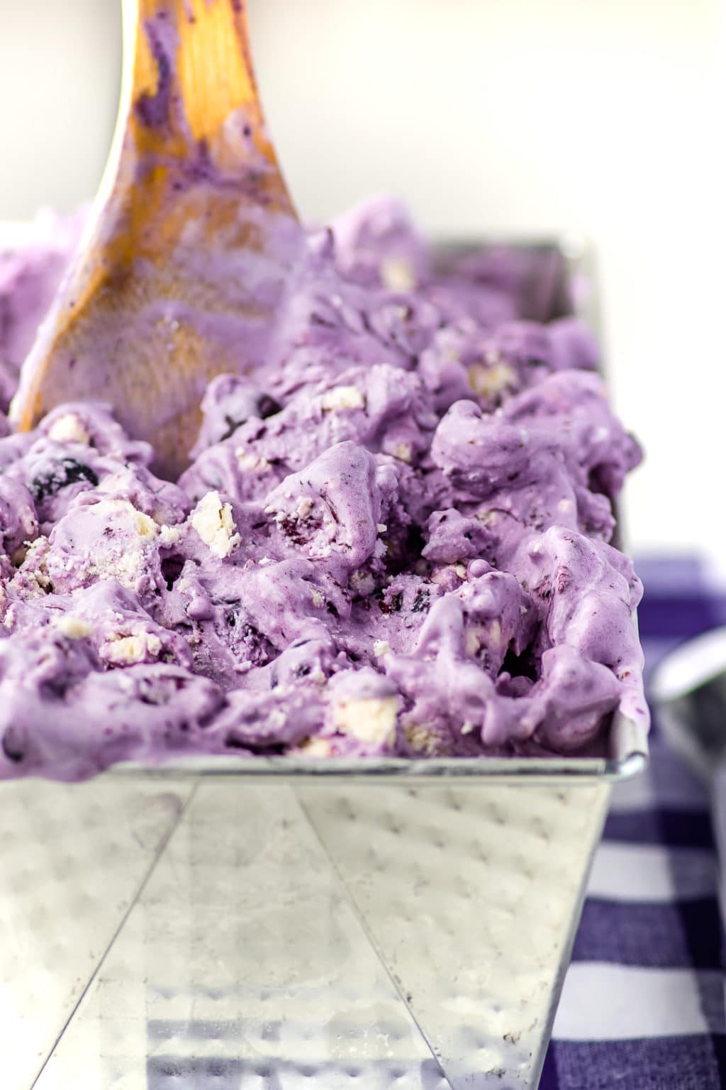 A bright lavender colored blueberry cheesecake ice cream in a silver loaf pan and wooden spoon