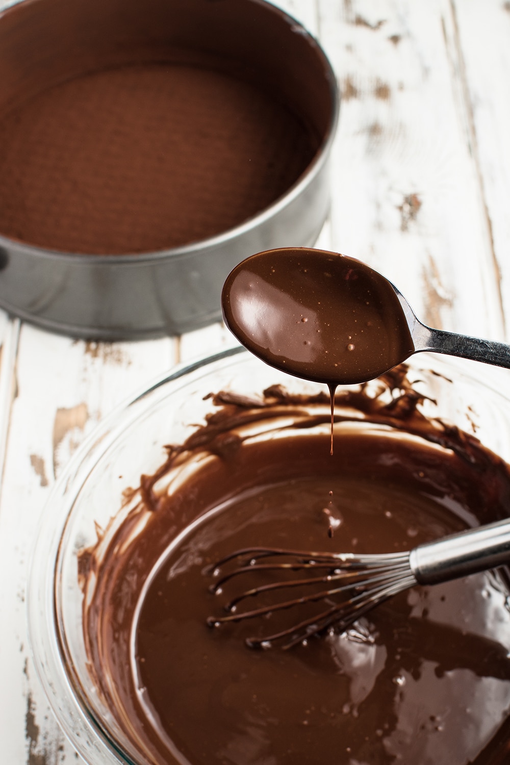 Bowl of melted chocolate with a dripping covered chocolate spoon on a rustic white wooden background 