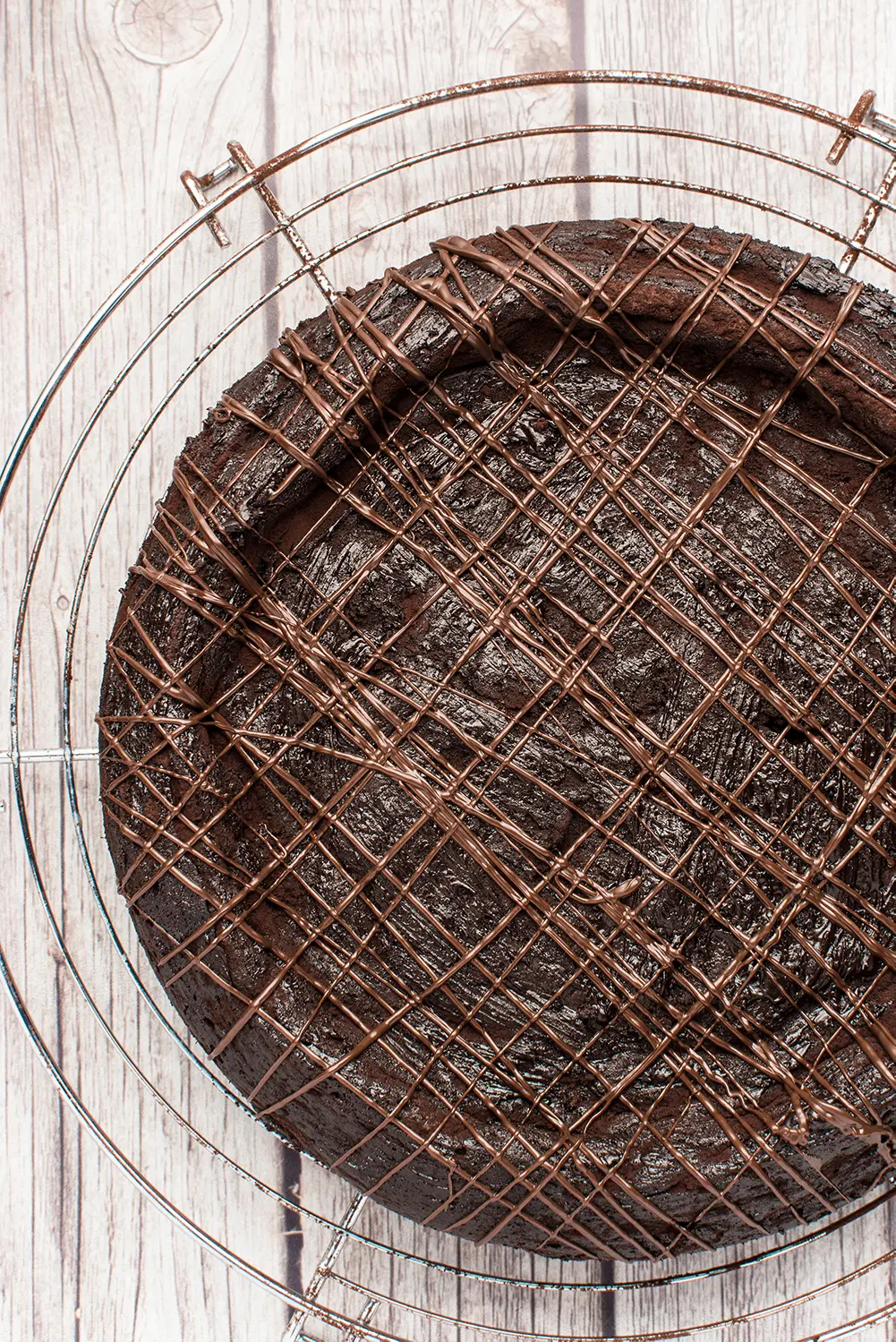 dark chocolate torte with stripes of melted chocolate resting on a round metal cooling rack 