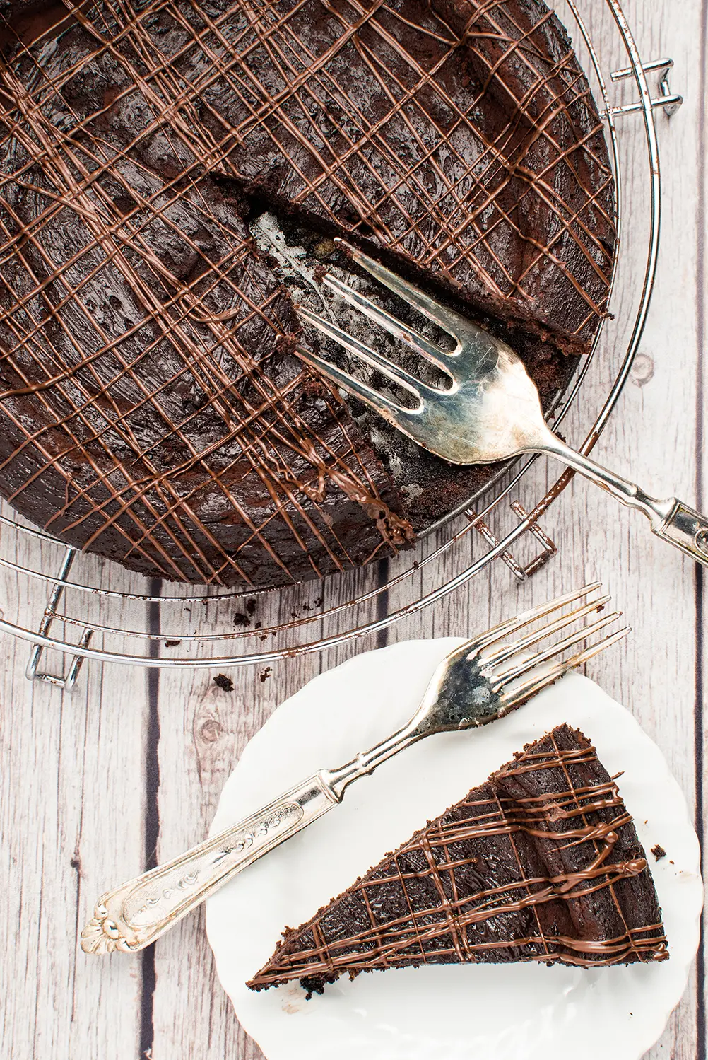 Chocolate torte on a metal cooling rack with a piece removed and placed on a small white plate
