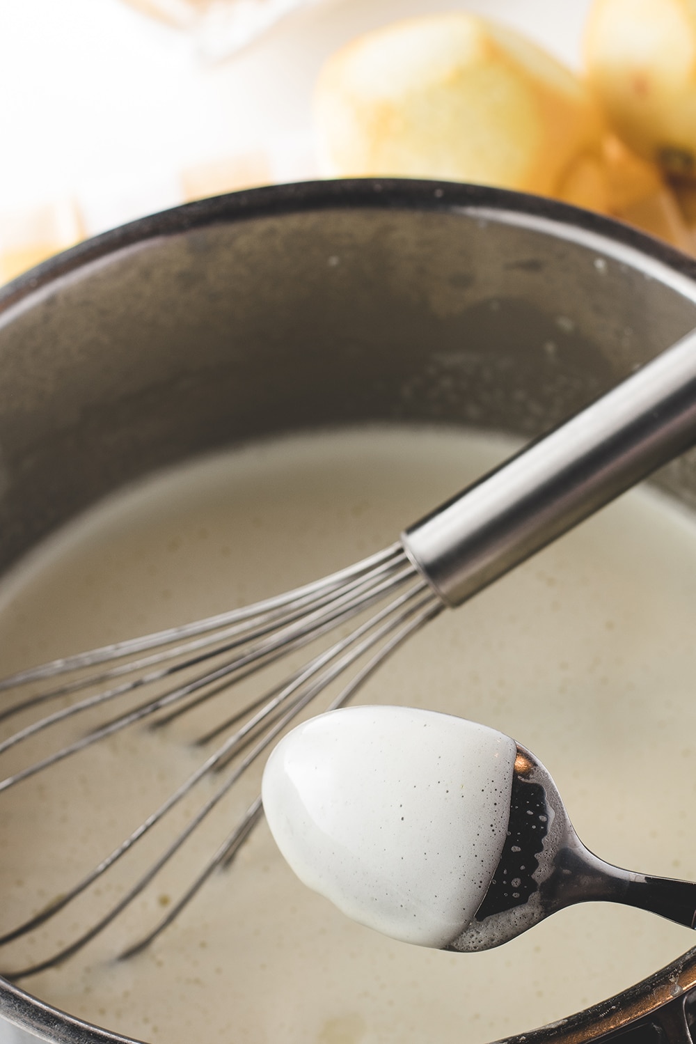A sauce pan with creamy mixture with a whisk and a coated spoon 