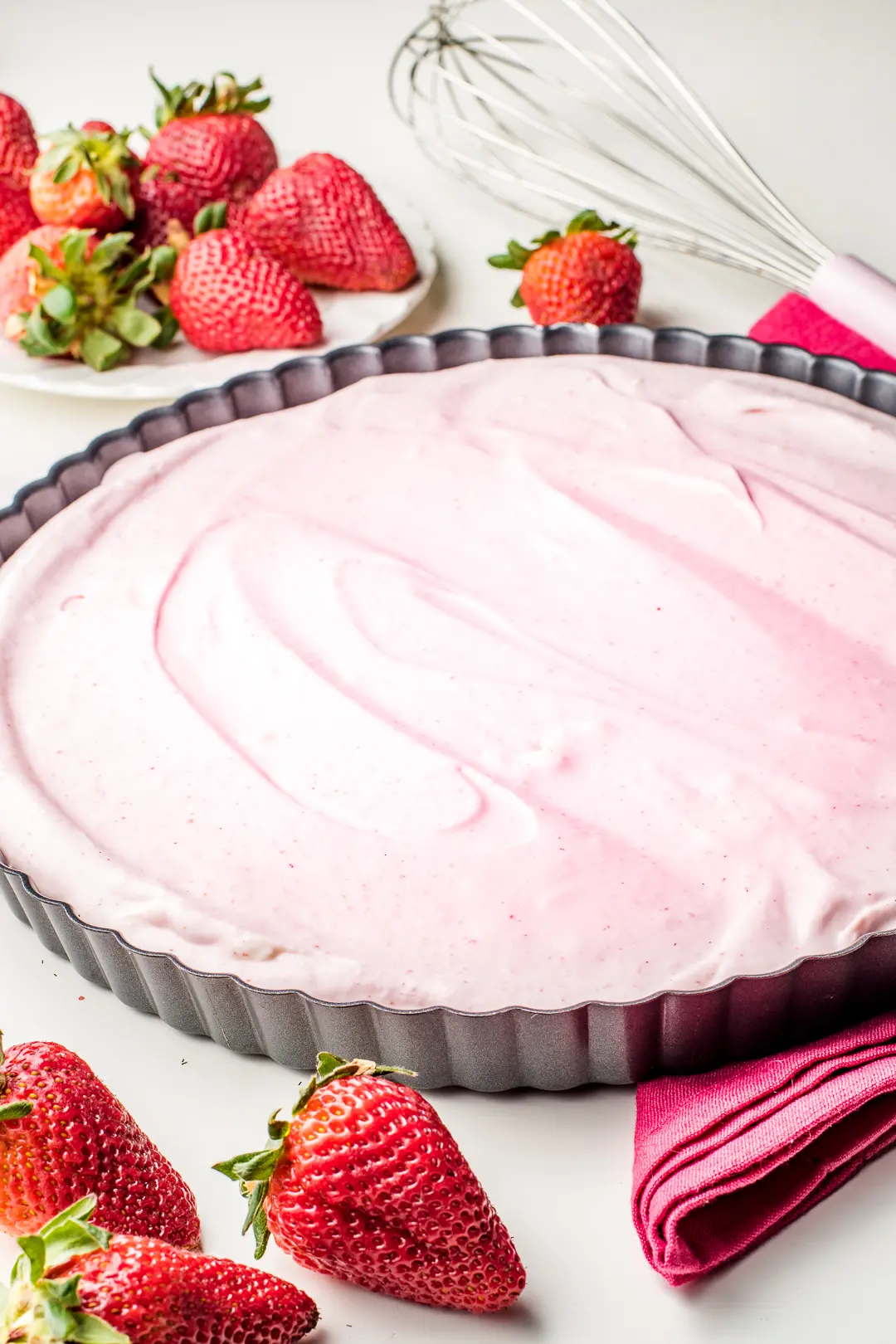 Strawberry cream pie filling inside of a tart pan surrounded by fresh strawberries