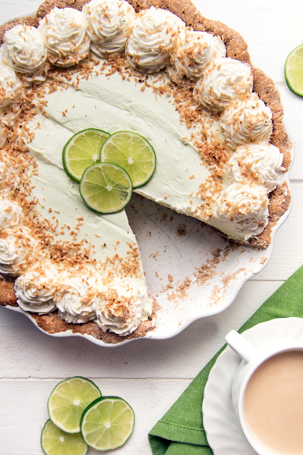 A no bake low carb key lime pie on a white background with slice limes and a white tea cup filled with fresh brewed tea.