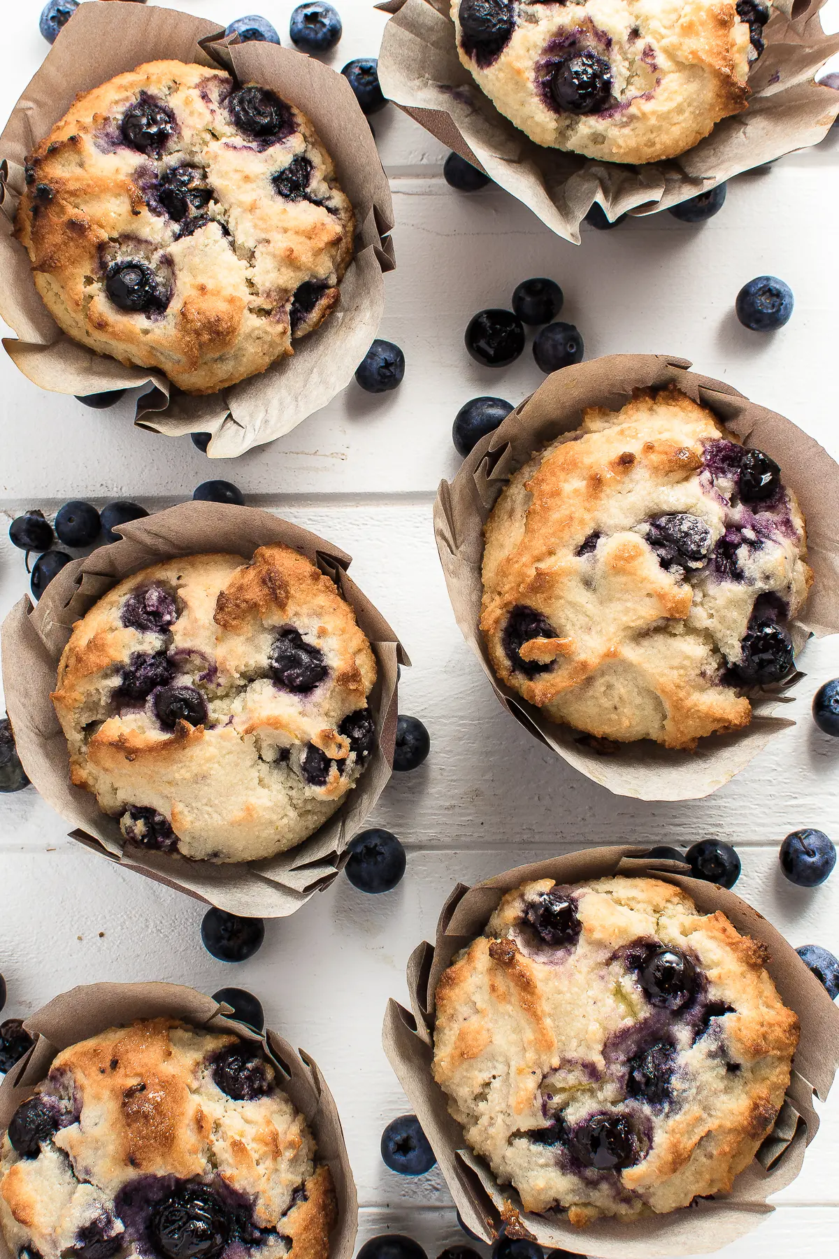 Blueberry muffins on a bright white wooden background with scattered fresh blueberries 