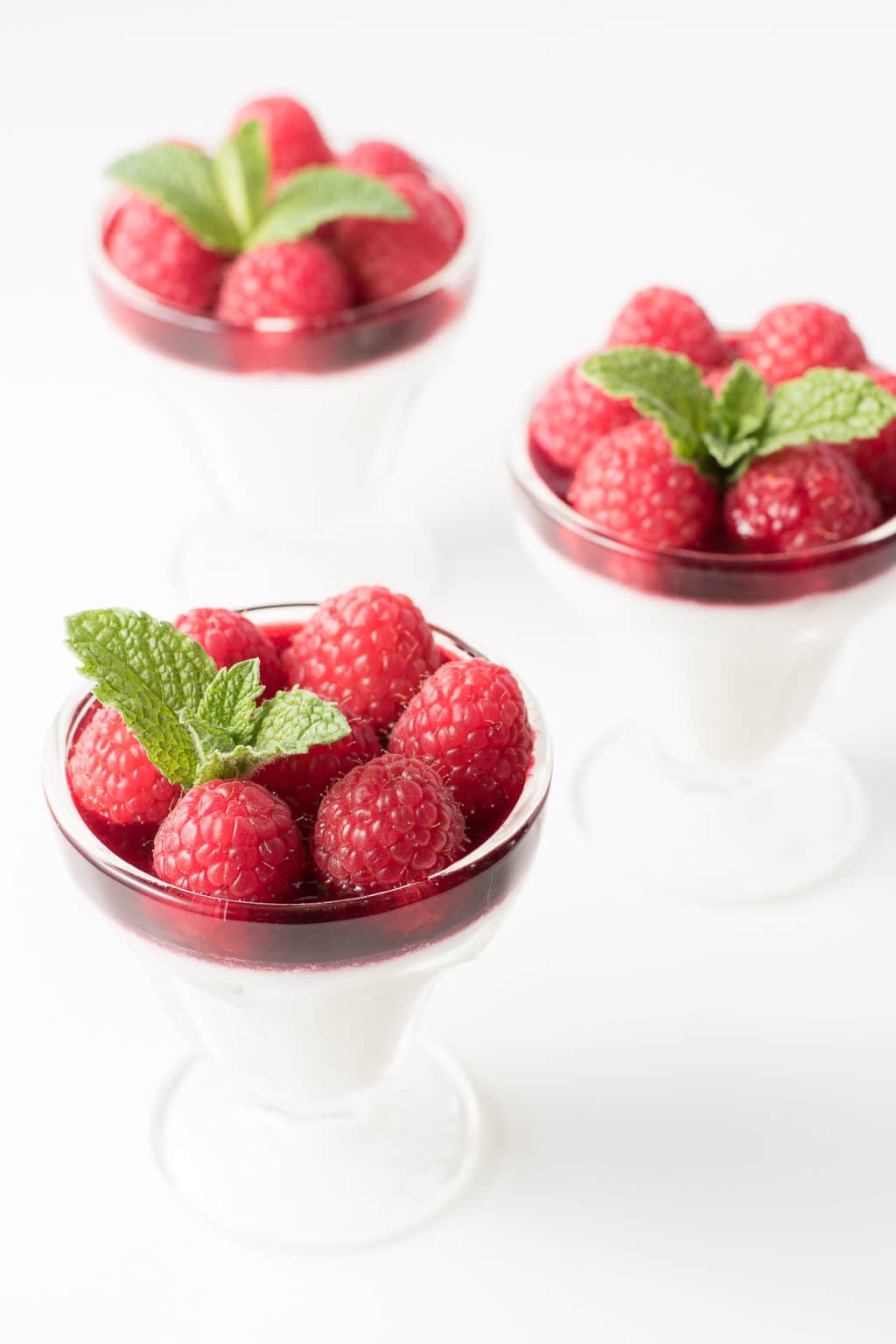 Three parfait glasses filled with Panna Cotta and topped with fresh raspberries and mint sprigs.