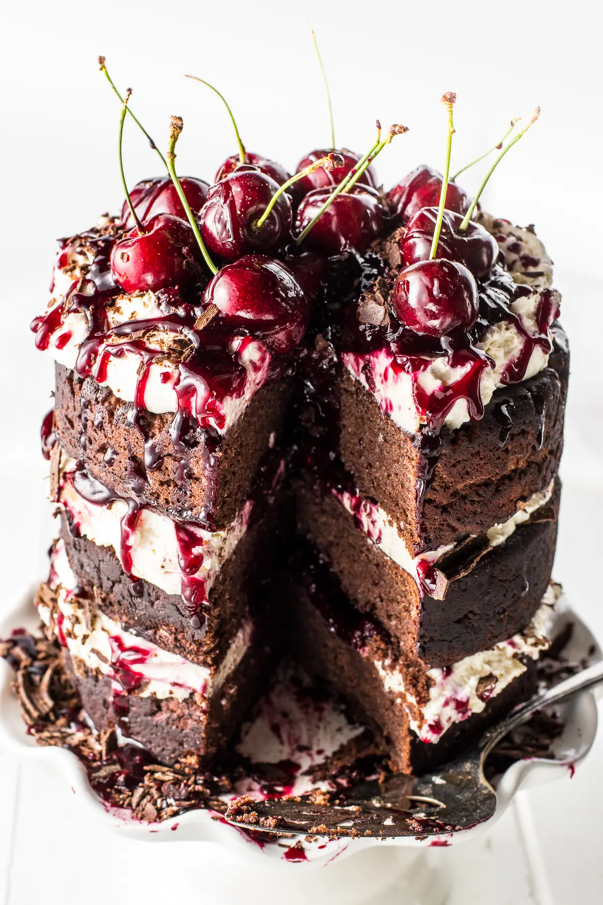 A gluten free black forest cake with a slice removed against a bright white background and wooden table