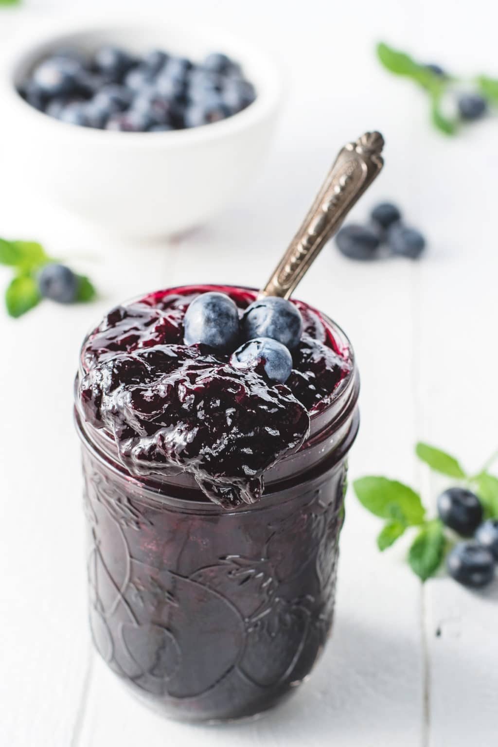 A jar of sugar-free blueberry jam with a large drip running down the side of the jar on a white background