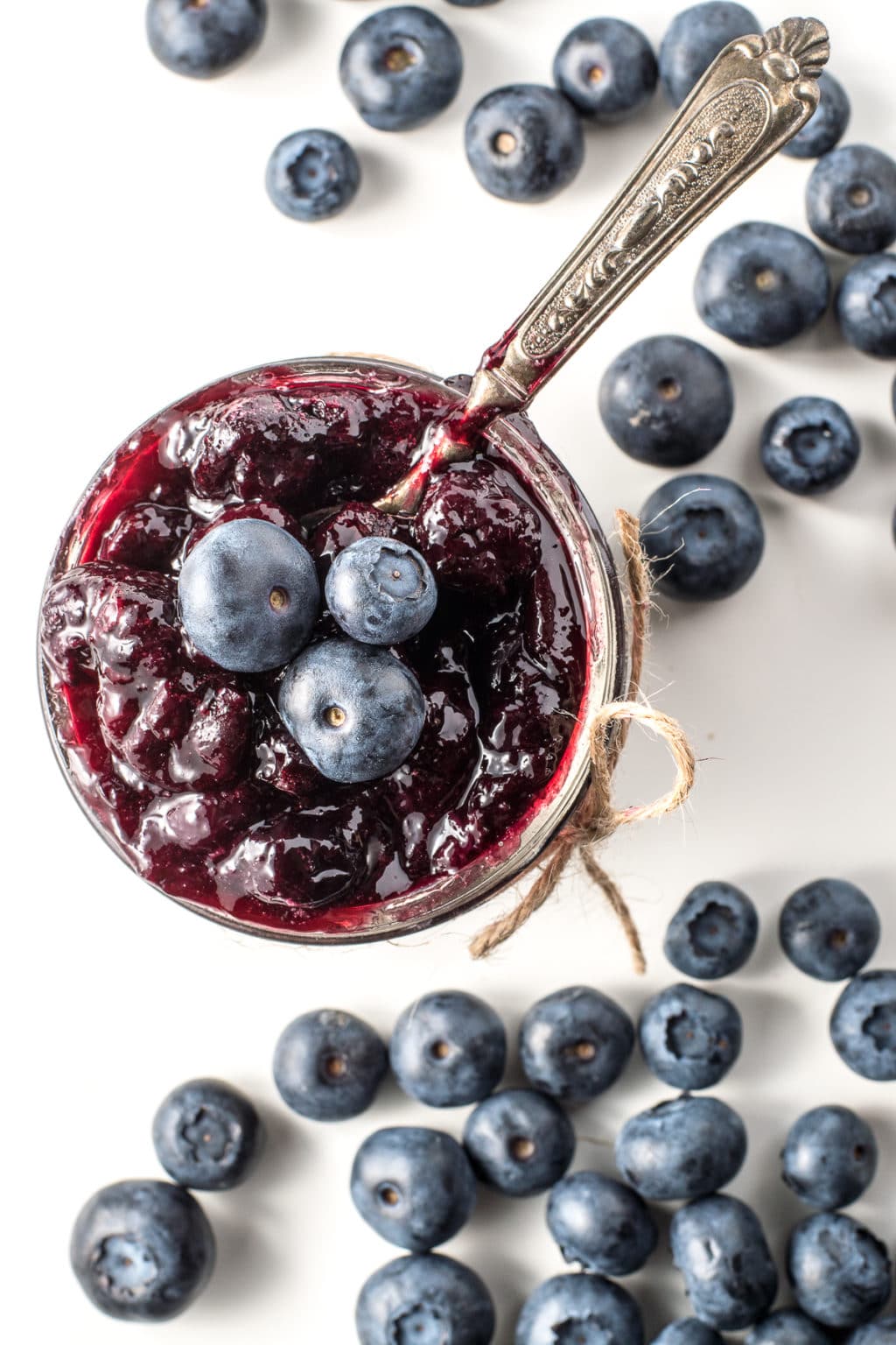 Top down view of an open jar of blueberry jam with scattered blueberries on a white background