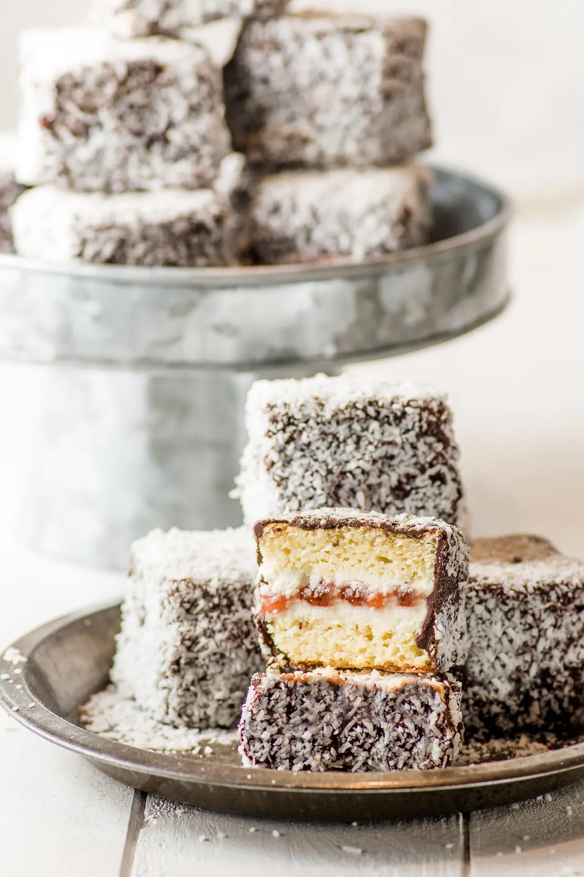Lamingtons stacked on a rustic pin tin on a white rustic wooden board.