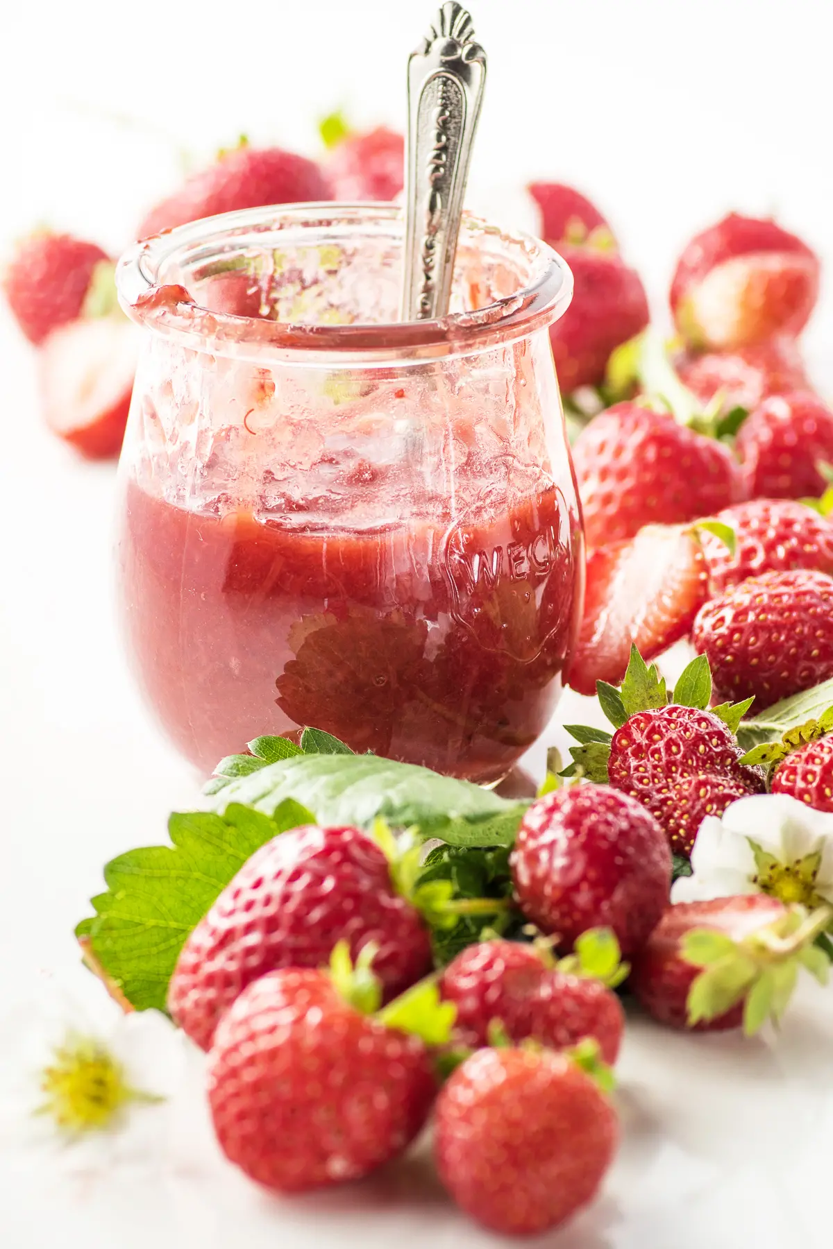 A jar of sugar free strawberry jam, with fresh strawberries piled around it.