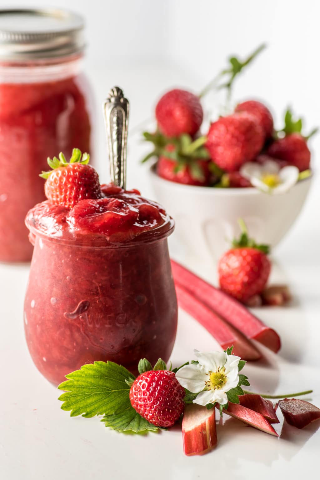 An overflowing jar of sugar-free strawberry rhubarb jam on a bright white background