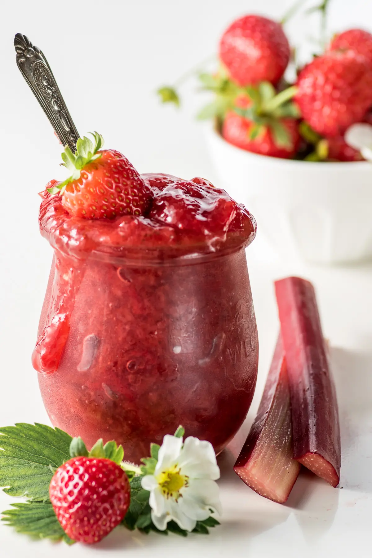 An overflowing jar of strawberry rhubarb jam on a bright white background