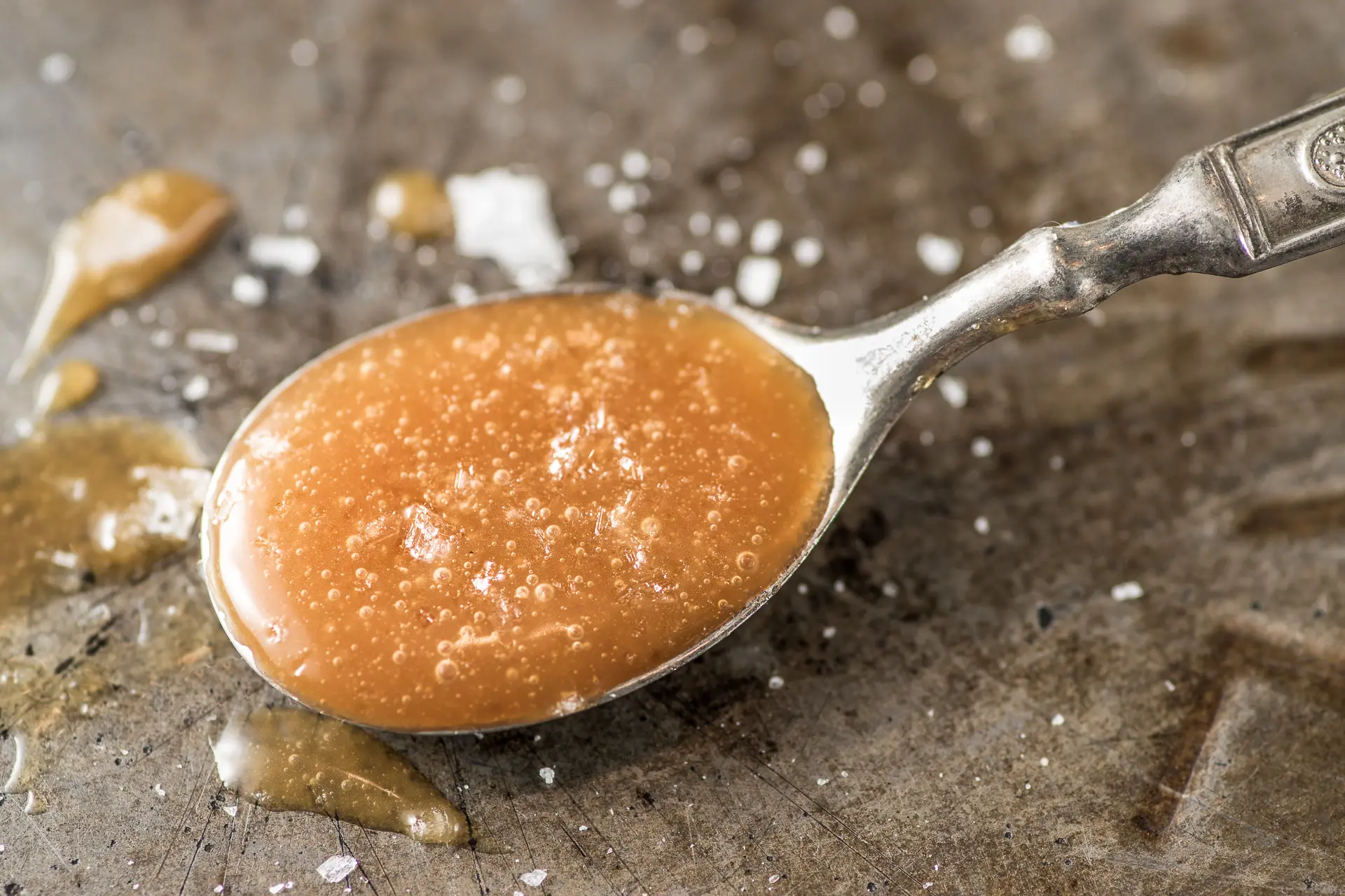 A spoonful of amber colored caramel sprinkled with corse salt on a rustic pie tin. 