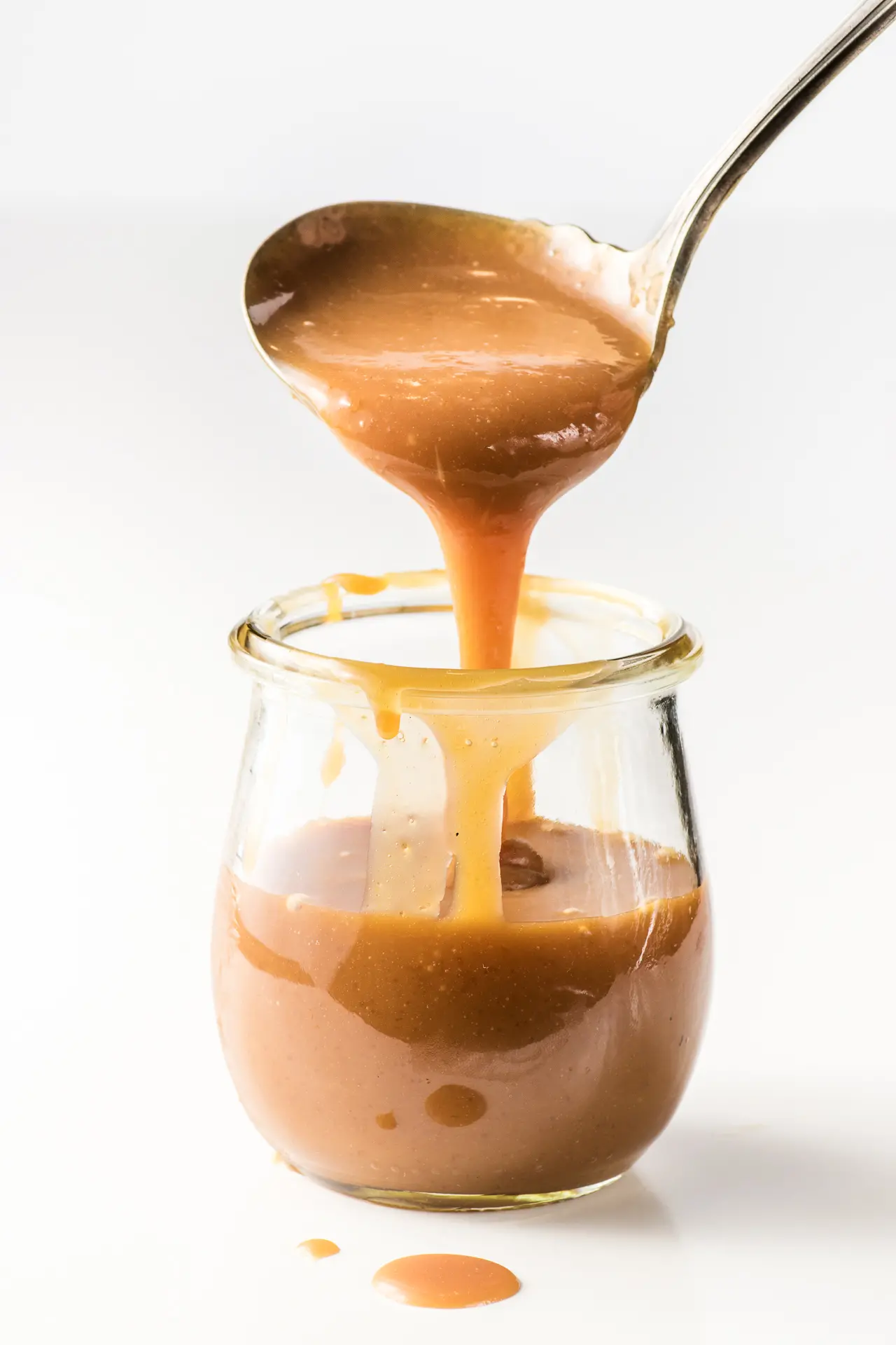 A small jar of keto caramel sauce. Caramel is being scooped out with a mini ladle.