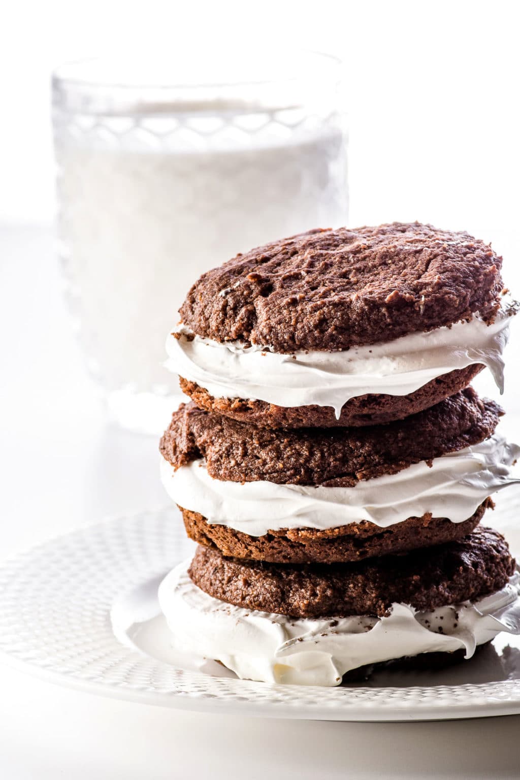 Stacked whoopie pies on a white plate in front of a glass of cashew milk