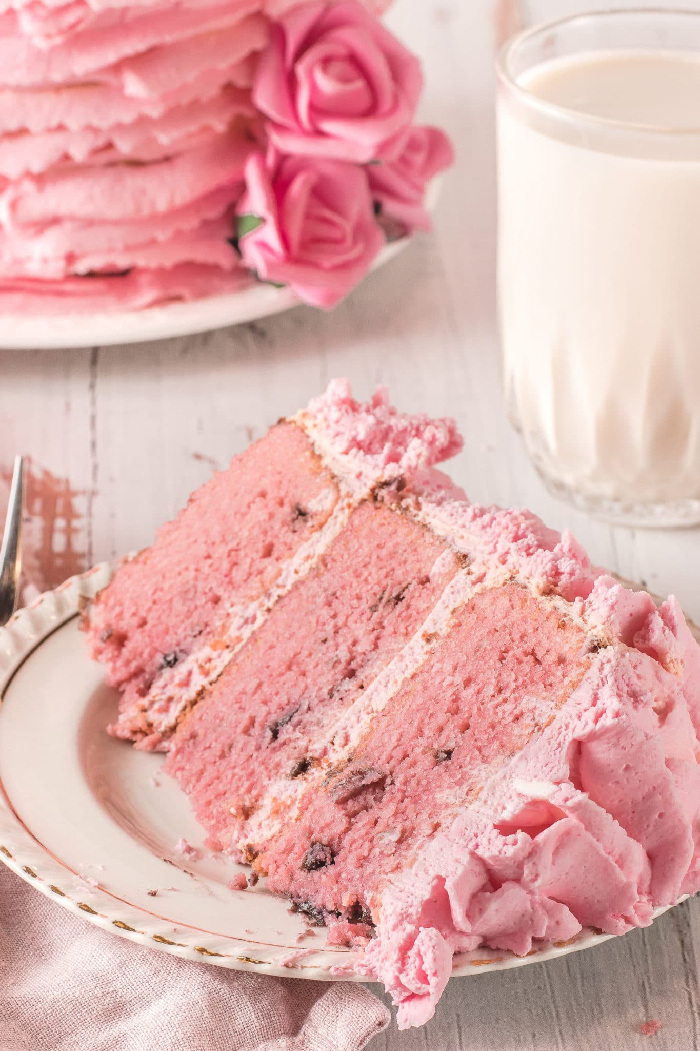 A big slice of pretty pink low carb cherry chip cake on a cream colored plate with gold rim.