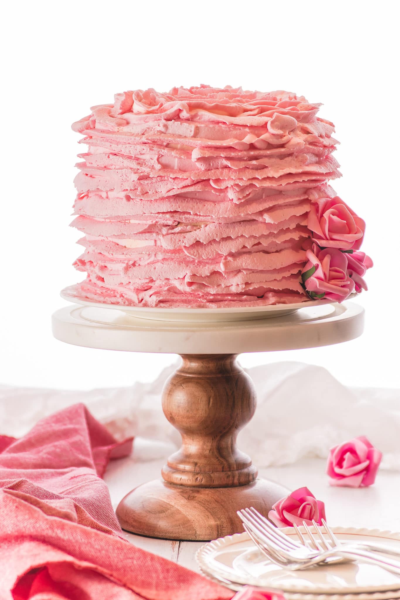 A pink ruffled cake on a marble and wooden cake against a bright white tabletop and background