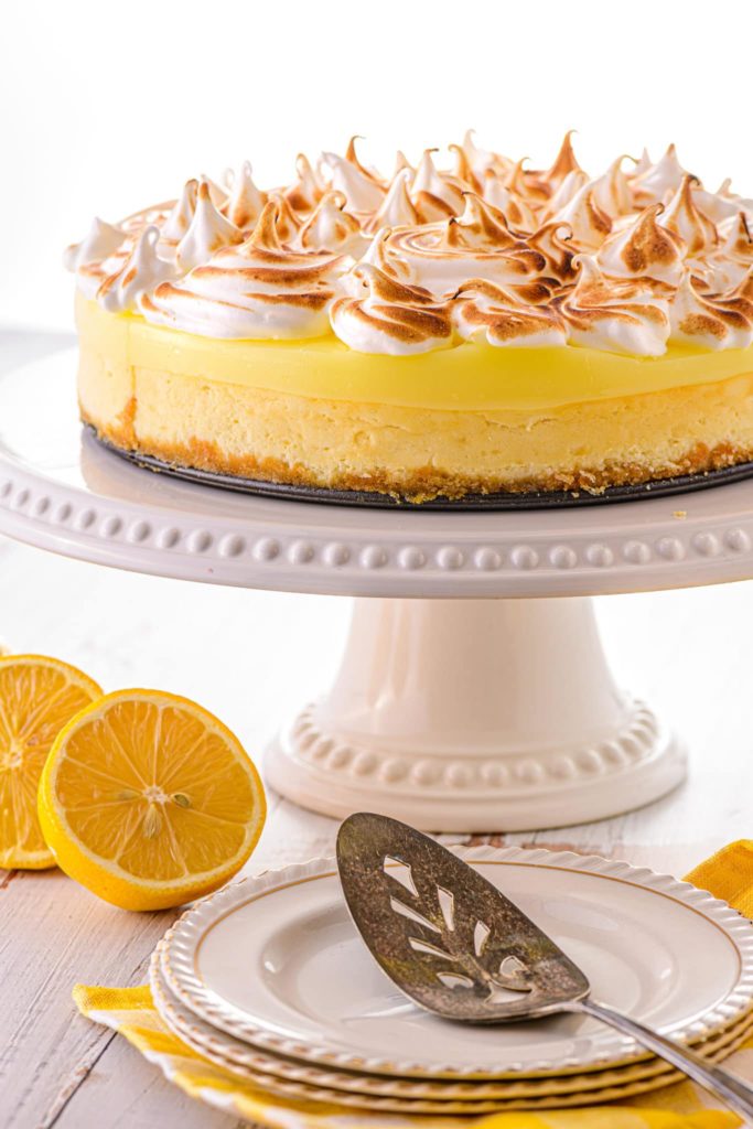 A low carb lemon cheesecake on a cake tray, with sliced lemons on the table nearby.