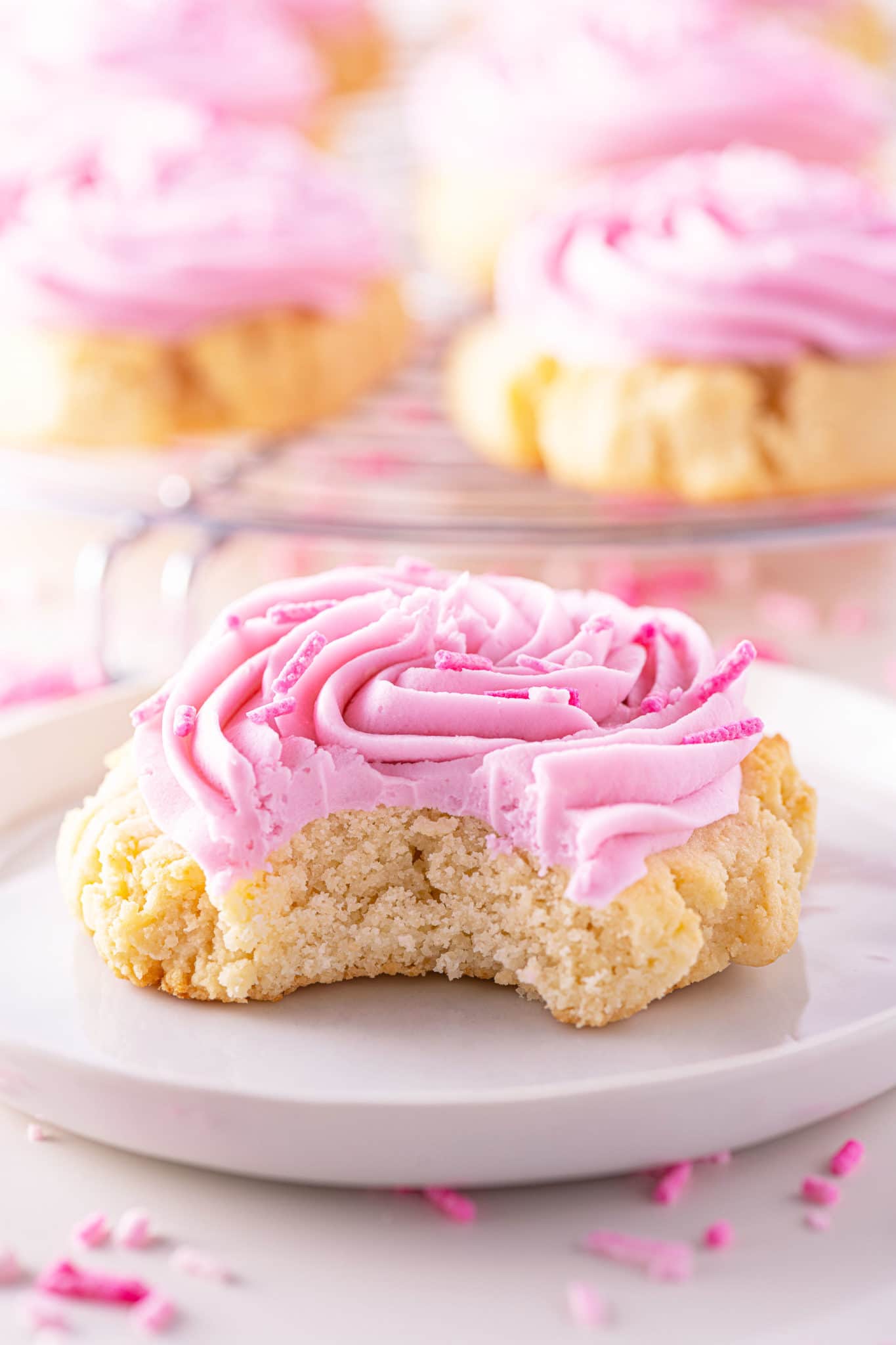 Vanilla keto sugar cookie with pink swirled frosting and pink sprinkles on a bright white plate.