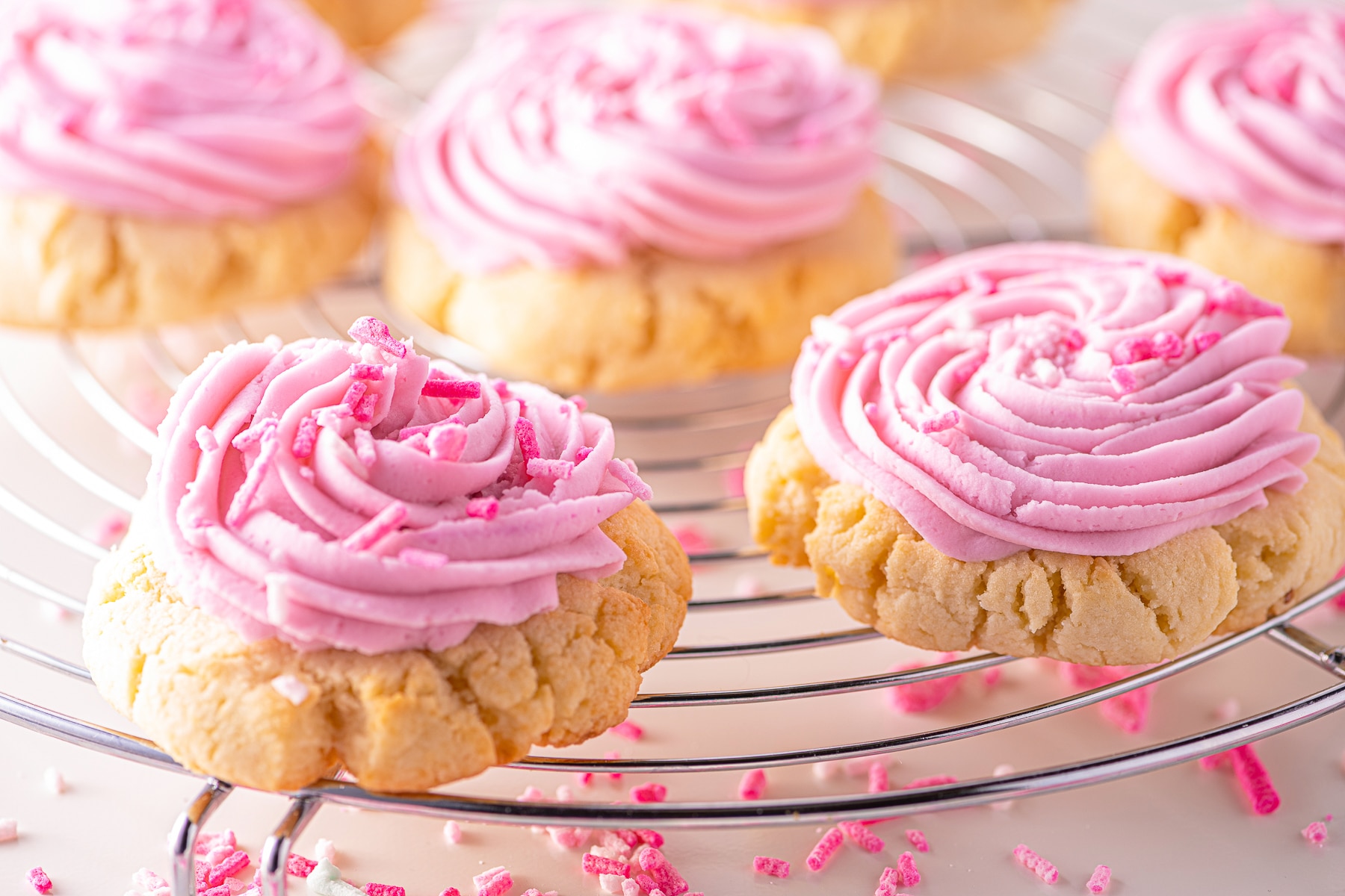 Keto sugar cookies topped with pink frosting on a cooling rack.