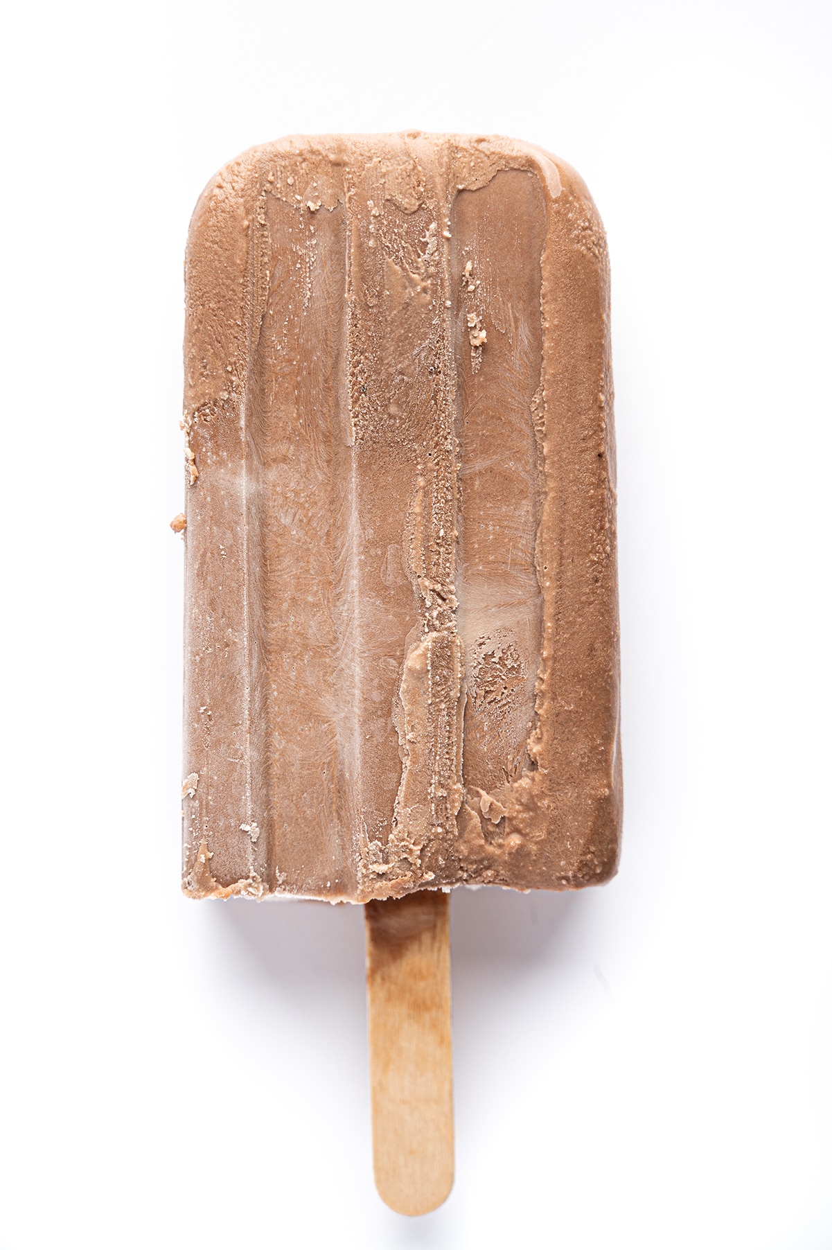 A single frozen sugar free fudgesicle with wooden stick against a bright white background