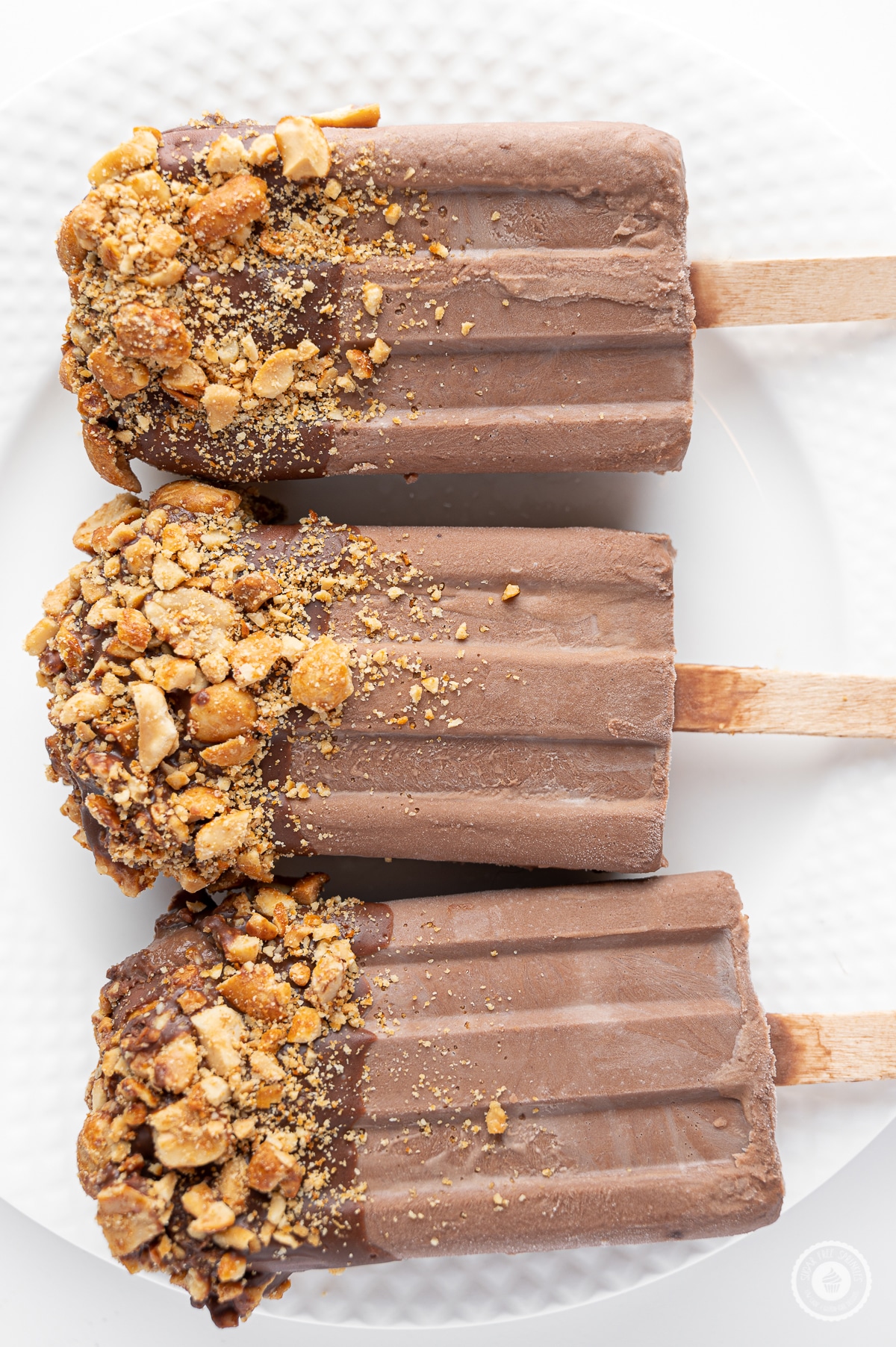 Three sugar free fudgesicles with chocolate topping and crushed peanuts on a bright white plate. 