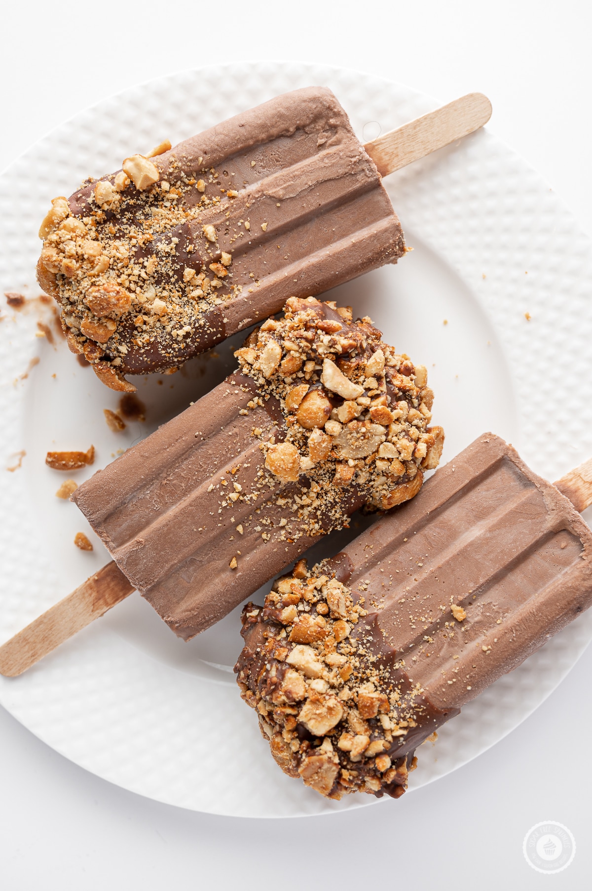 Sugar free fudgesicle with tops coated in milk chocolate and crushed peanuts on a bright white background 