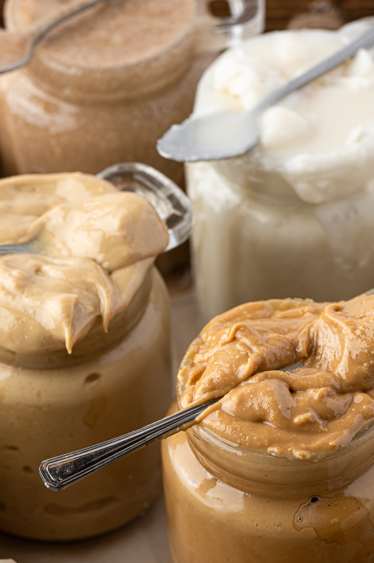 Jars of nut butters with small spoons laying across the top jar opening