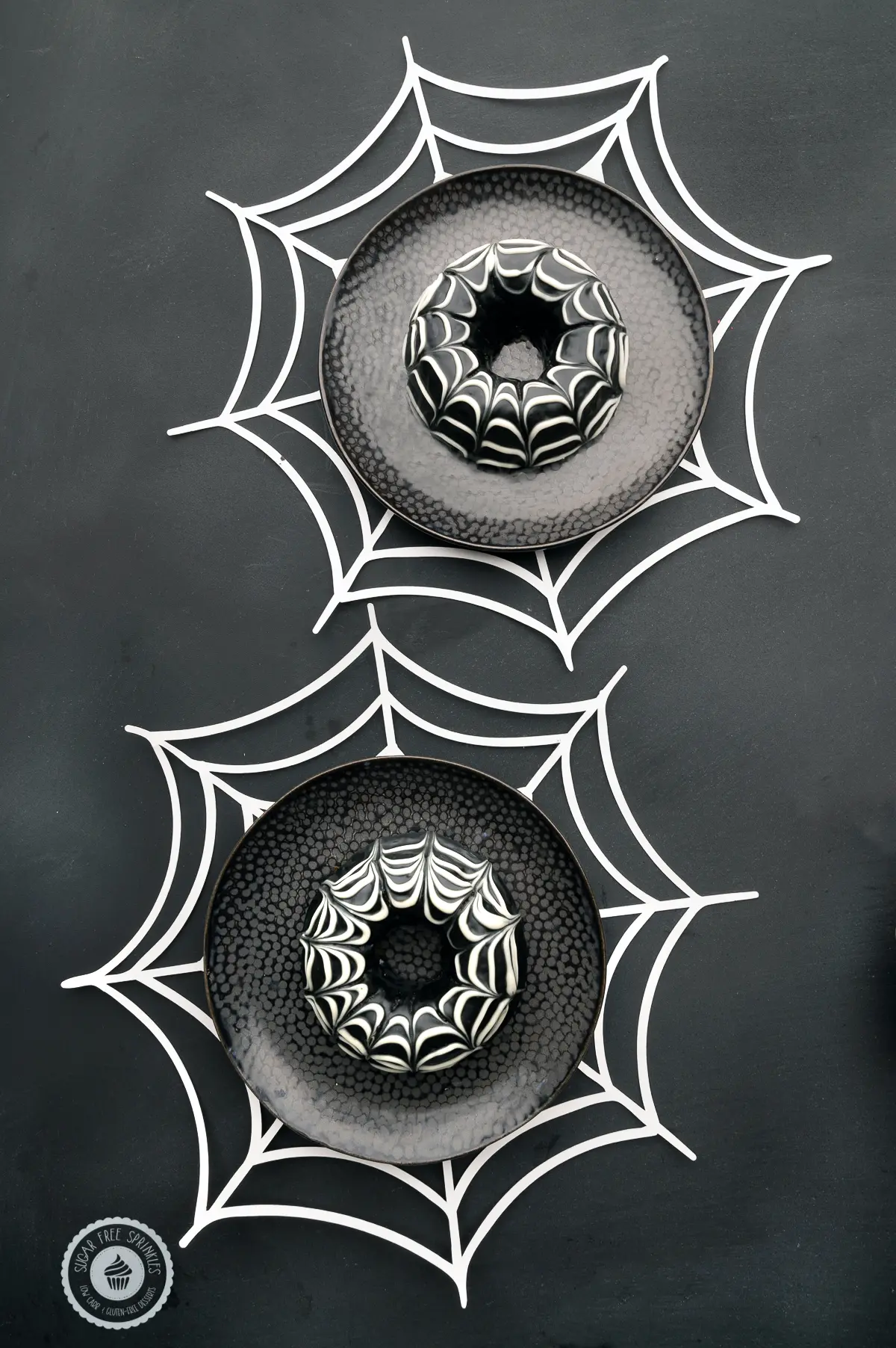 Chocolate glazed keto donuts with a spider web design on dark black plates with white paper spider webs 