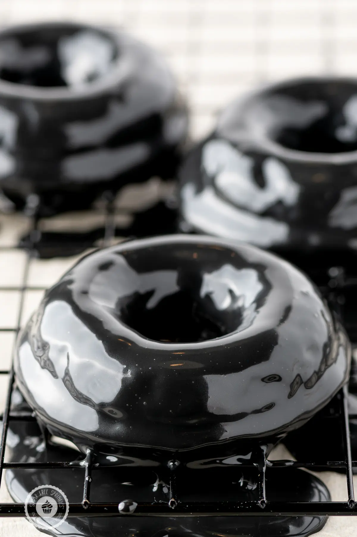 Black shiny ganache coated donuts on a cooling rack 