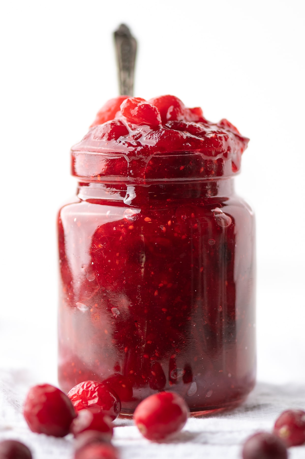 A jar filled with bright red sugar free cranberry jelly.  Cranberries are scattered around the bottom. 