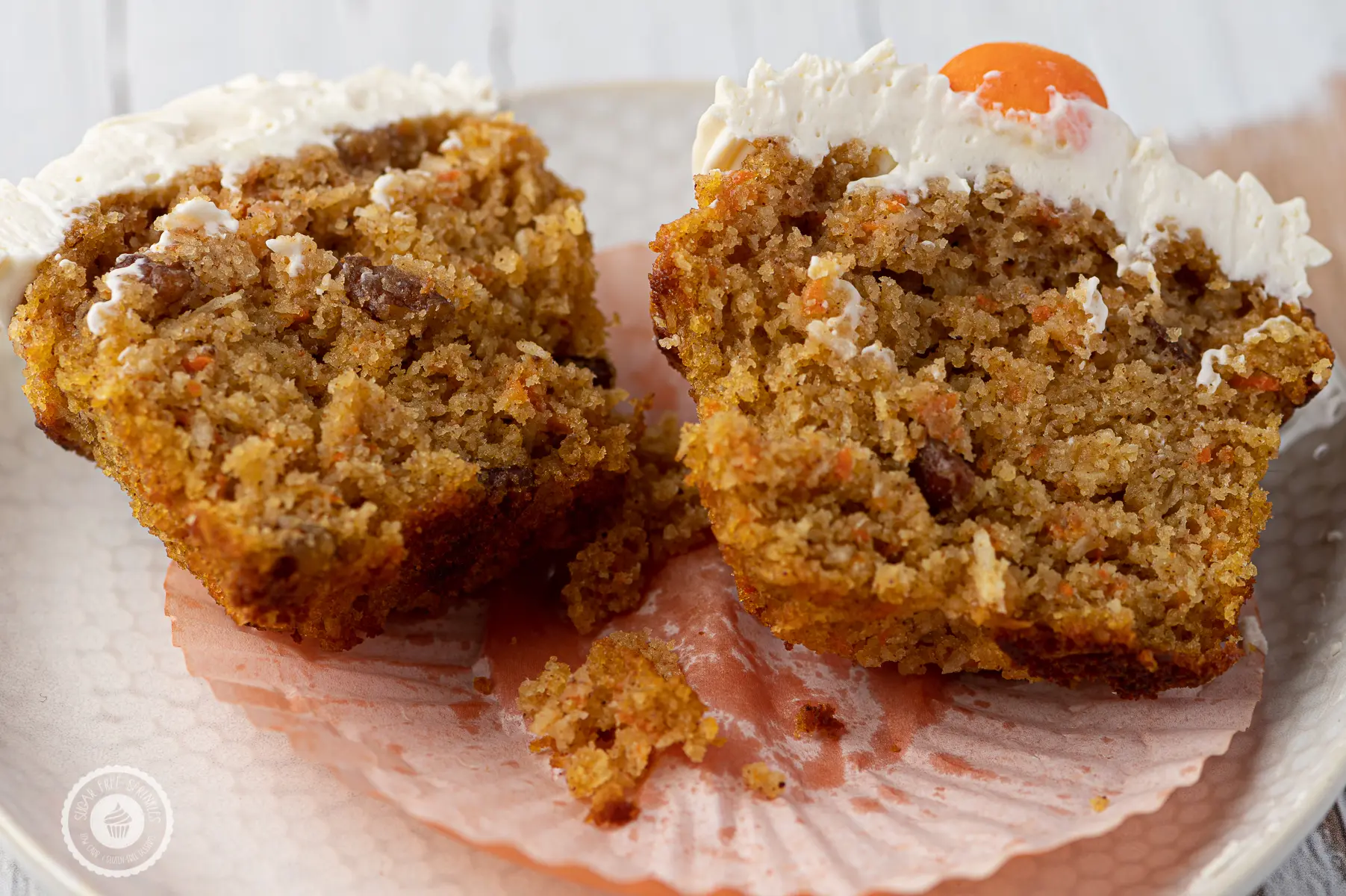 A carrot cake muffin with cream cheese frosting cut down the center and place on a white textured plate. 