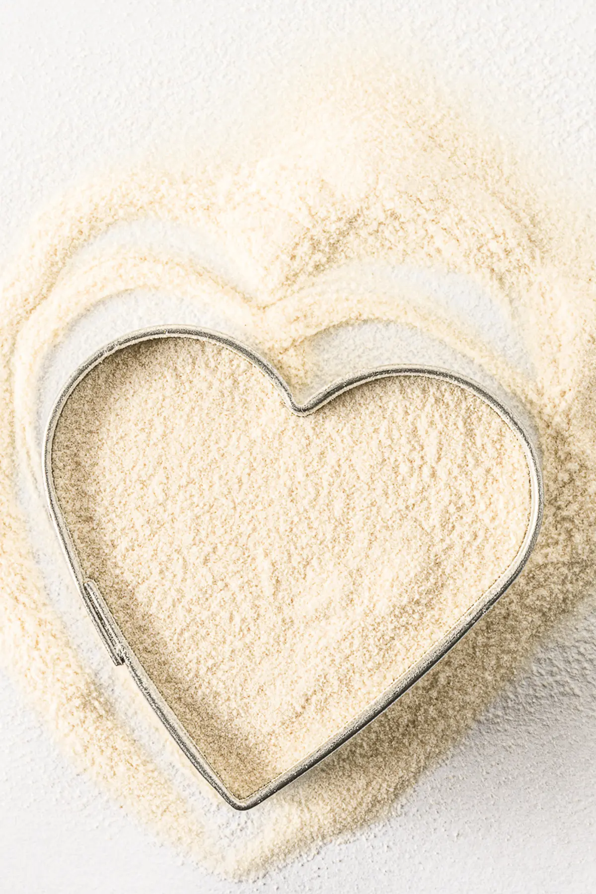 Xanthan gum poured in an around a heart shaped cookie cutter on a bright white background. 
