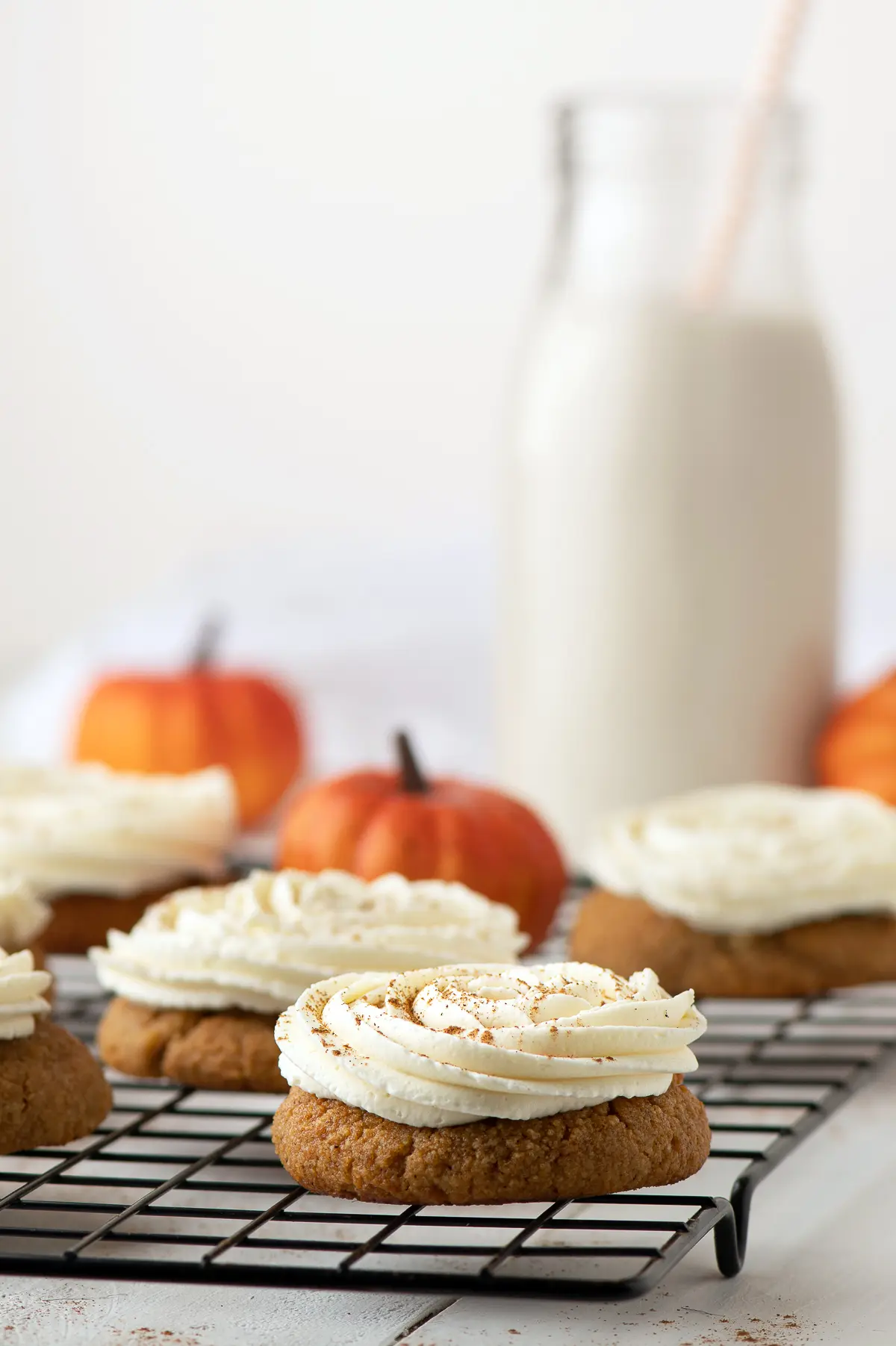  Pumpkin spice cookie with a swirl of cream cheese frosting.  Mini pumpkins are in the background. 
