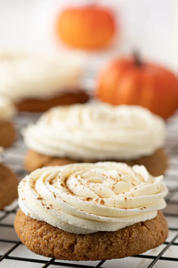 A low carb pumpkin cookie with a swirl of cream cheese frosting.  Mini pumpkins are in the background. 