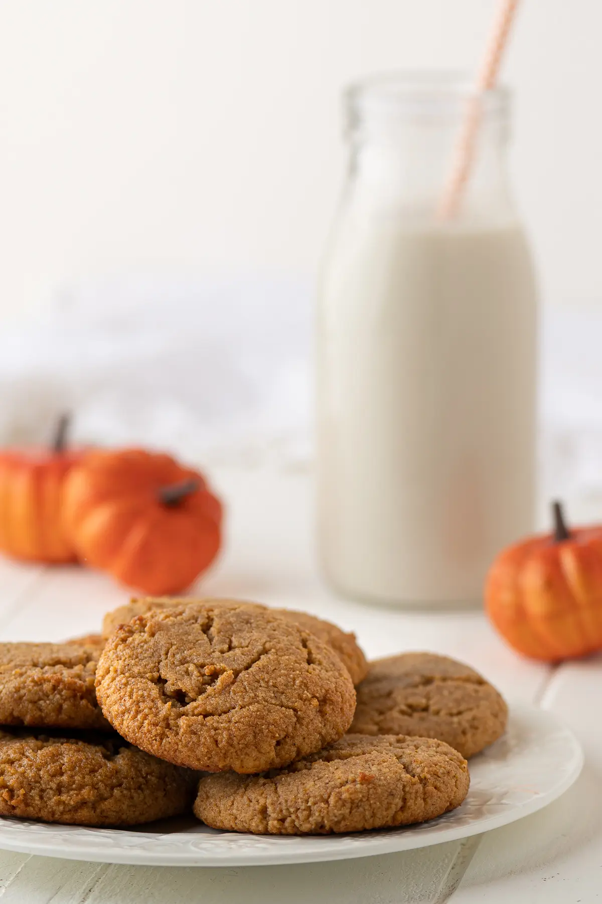 Pumpkin cookies on a white plate with a glass of almond milk and mini orange pumpkins in the background