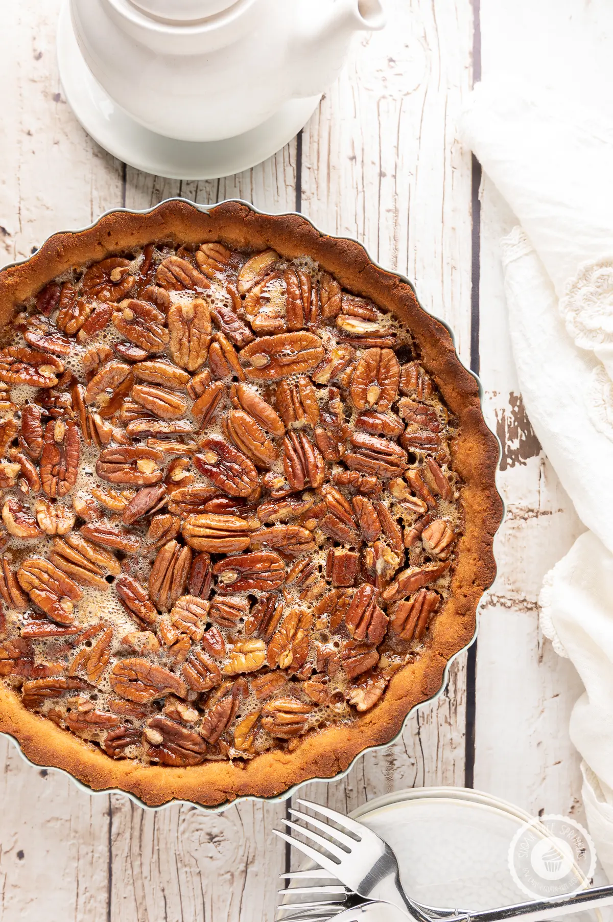 Pecan pie on a rustic wooden backdrop with white napkin, plates and a pot of hot tea
