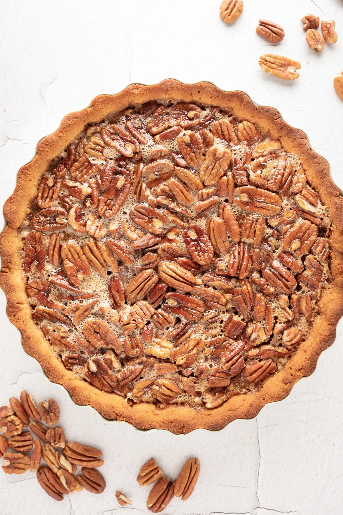 sugar-free pecan pie on a bright white back ground with scattered raw pecans. 