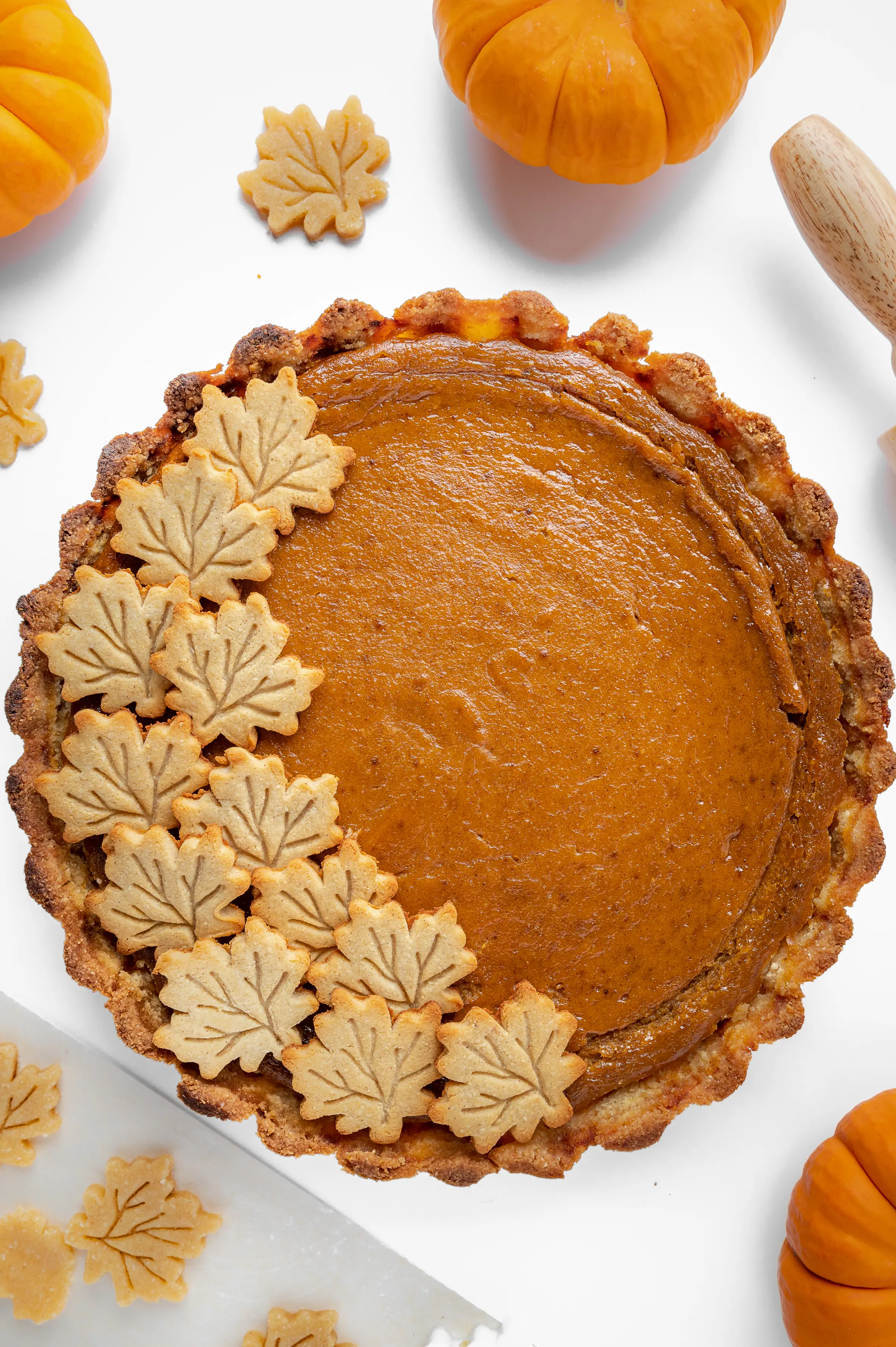 Top down view of a sugar free pumpkin pie, with maple leaf-shaped sugar cookies decorating one side.